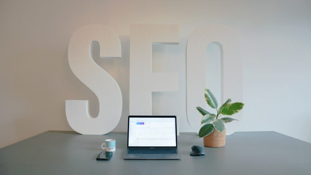 Modern and organized workspace in an SEO agency, featuring a sleek office desk with large SEO letters in the background. The desk is ready for productivity, with an espresso, a mobile phone, and a small plant neatly arranged. The absence of a person creates a calm, inviting environment, perfect for focused work in the digital marketing space.